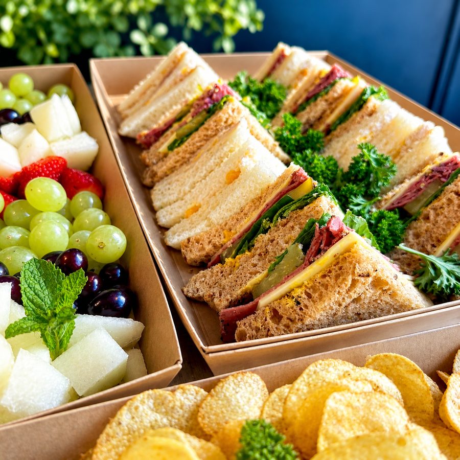 A Roosters catering box — assorted sandwich rounds, fruit salad, crisps