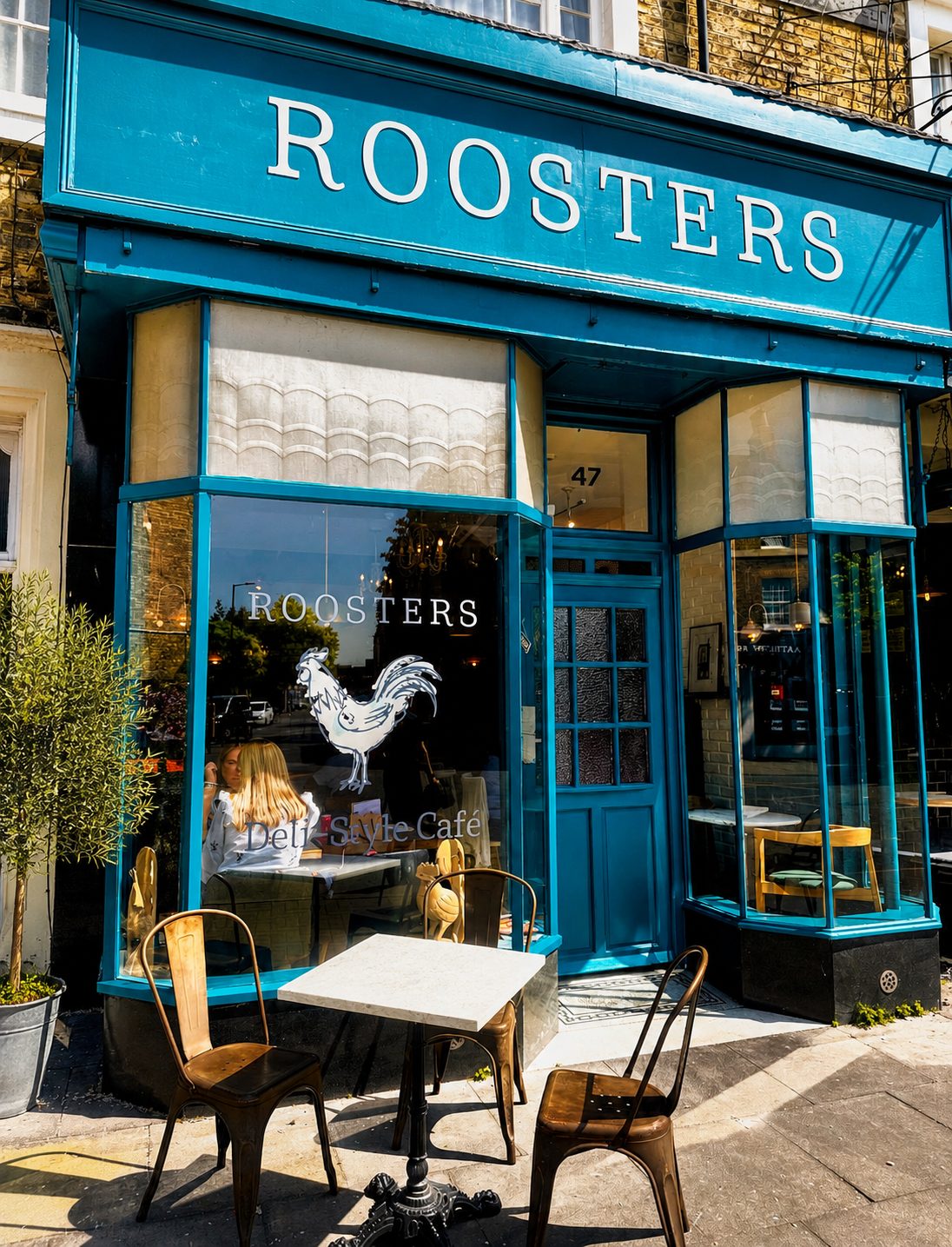 The teal Roosters shopfront on St Cuthbert’s Street, Bedford — bistro chairs out front, the rooster decal in the window